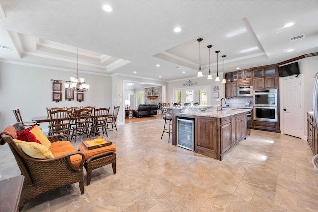 kitchen with a center island with sink, visible vents, stainless steel double oven, wine cooler, and a raised ceiling