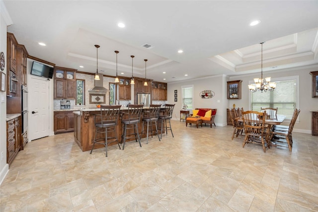 kitchen featuring a wealth of natural light, a tray ceiling, visible vents, and wall chimney range hood