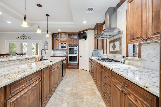 kitchen featuring brown cabinetry, visible vents, a tray ceiling, appliances with stainless steel finishes, and wall chimney range hood