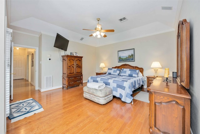 bedroom with crown molding, visible vents, a raised ceiling, and light wood-type flooring