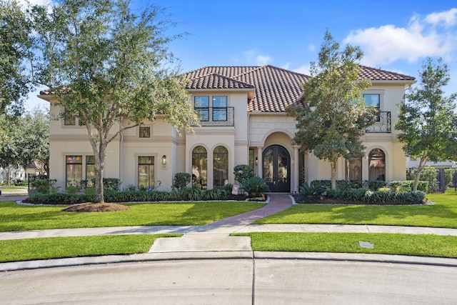 mediterranean / spanish-style home featuring a balcony, stucco siding, a tile roof, and a front lawn