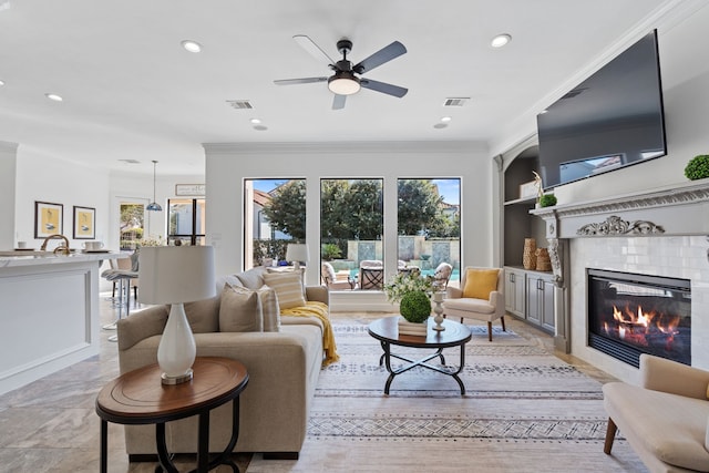 living area featuring crown molding, built in features, visible vents, and a tile fireplace