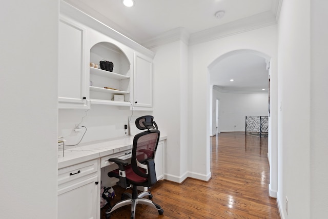 office area with arched walkways, built in study area, crown molding, and wood finished floors