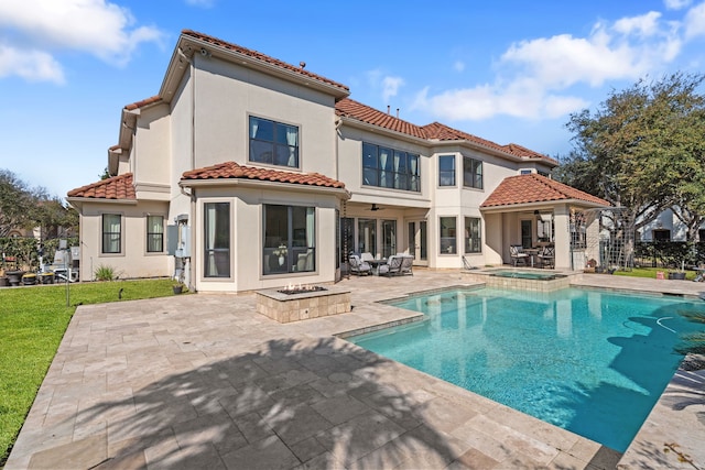 rear view of property featuring a patio, a ceiling fan, stucco siding, a fire pit, and a tiled roof