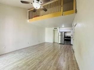 unfurnished living room featuring ceiling fan, wood finished floors, and a towering ceiling