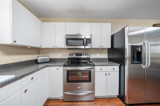 kitchen featuring stainless steel appliances, dark countertops, and white cabinetry