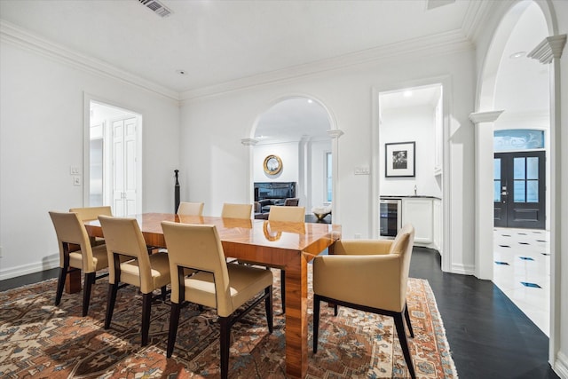 dining area featuring arched walkways, wine cooler, visible vents, and crown molding