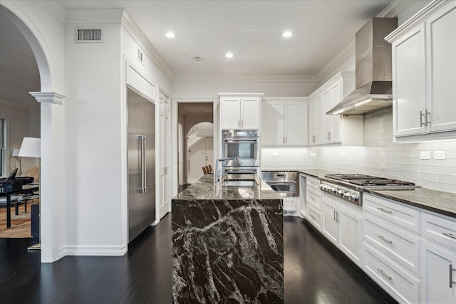 kitchen with arched walkways, stainless steel appliances, a sink, visible vents, and wall chimney range hood