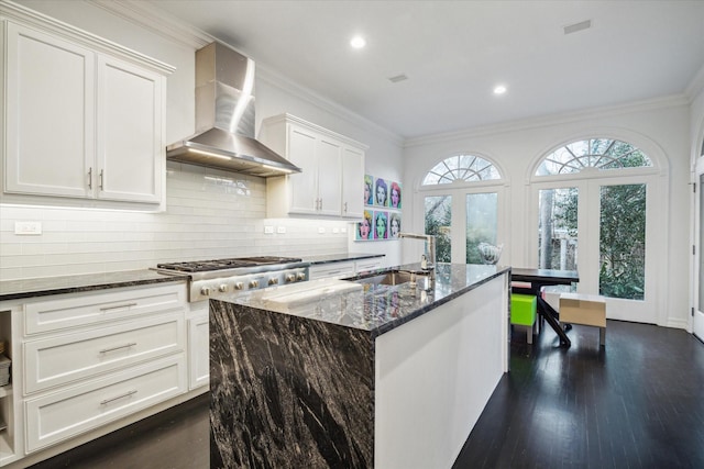 kitchen featuring stainless steel gas cooktop, a sink, wall chimney exhaust hood, dark stone countertops, and crown molding