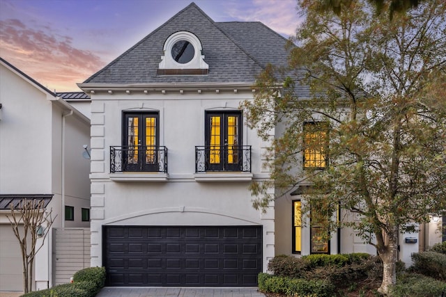 french country style house with a balcony, a garage, french doors, decorative driveway, and stucco siding