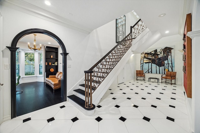 foyer with arched walkways, a notable chandelier, crown molding, decorative columns, and stairway