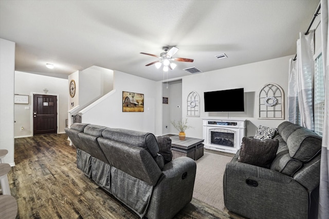 living room with dark wood-style floors, ceiling fan, visible vents, and a fireplace with raised hearth