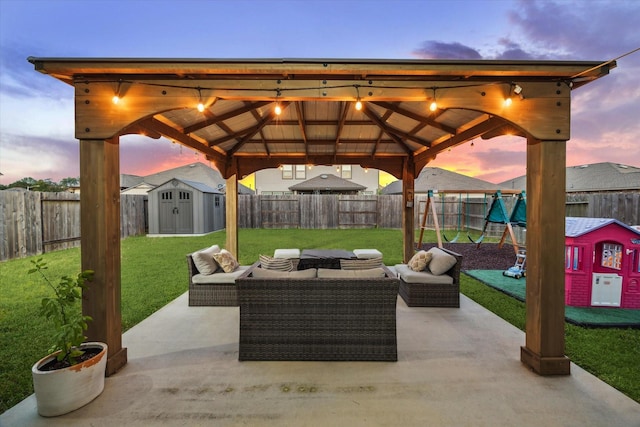 patio terrace at dusk featuring an outbuilding, a fenced backyard, a lawn, and a storage unit