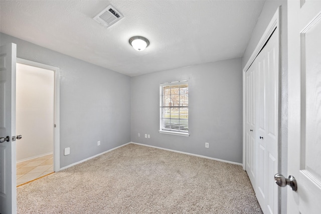 unfurnished bedroom with baseboards, visible vents, a textured ceiling, carpet floors, and a closet