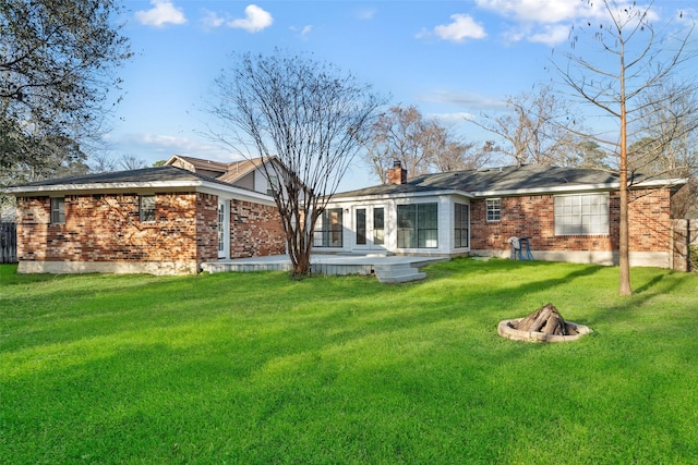 back of house with a yard, brick siding, an outdoor fire pit, and a chimney