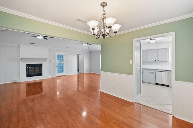 unfurnished living room featuring light wood-type flooring, a fireplace, crown molding, and ceiling fan with notable chandelier