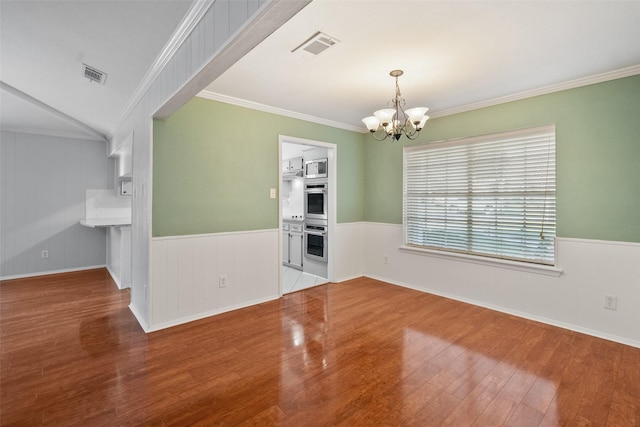 empty room with crown molding, wood finished floors, visible vents, and a notable chandelier