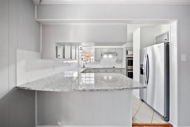 kitchen featuring light tile patterned floors, a peninsula, a sink, stainless steel appliances, and backsplash