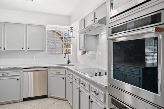 kitchen with light tile patterned floors, under cabinet range hood, stainless steel appliances, a sink, and decorative backsplash