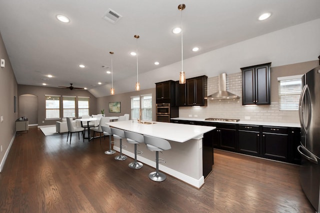 kitchen featuring visible vents, decorative backsplash, appliances with stainless steel finishes, open floor plan, and wall chimney exhaust hood