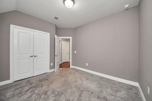 unfurnished bedroom with carpet, lofted ceiling, a closet, visible vents, and baseboards