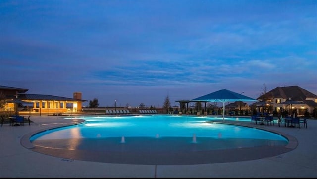 pool at dusk with a patio and a community pool