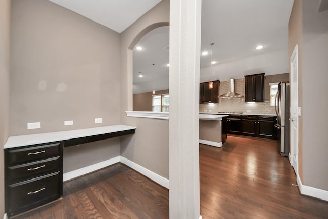 kitchen with dark wood-type flooring, freestanding refrigerator, wall chimney range hood, and decorative backsplash