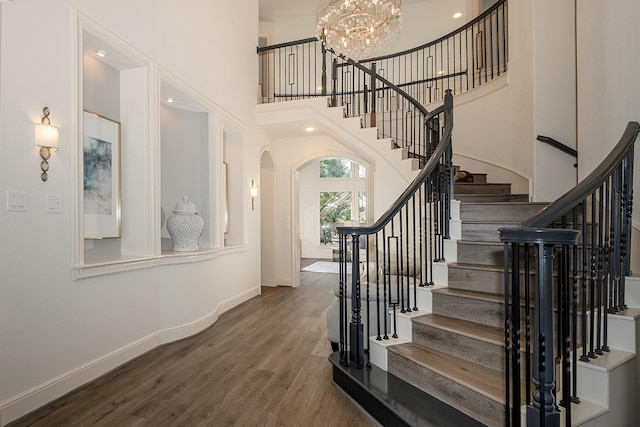 stairway with baseboards, arched walkways, wood finished floors, an inviting chandelier, and a high ceiling