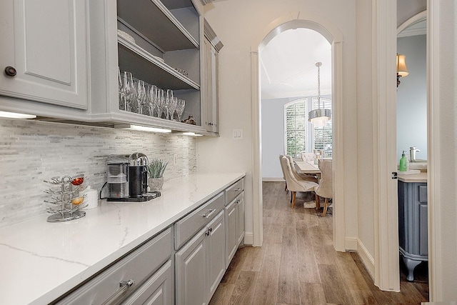 bar featuring light wood-type flooring, baseboards, arched walkways, and decorative backsplash