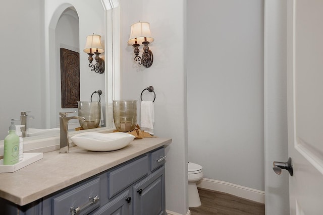 half bathroom featuring toilet, baseboards, wood finished floors, and vanity