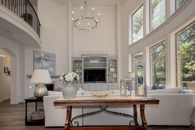 living area with a chandelier, a wealth of natural light, crown molding, and a towering ceiling