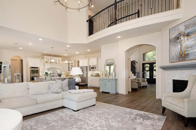 living room featuring arched walkways, dark wood-style flooring, a tiled fireplace, and a towering ceiling