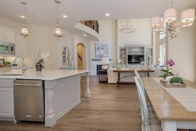 kitchen with a fireplace, stainless steel microwave, open floor plan, a sink, and wood finished floors