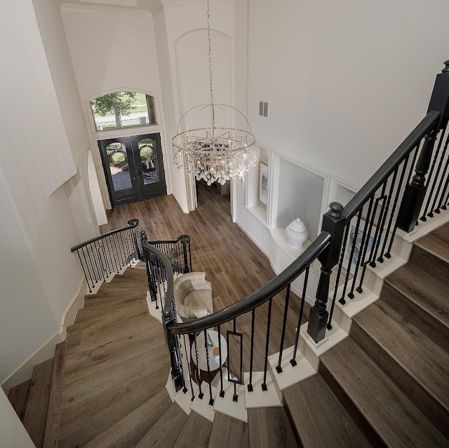 stairway with a chandelier, wood finished floors, visible vents, a towering ceiling, and french doors