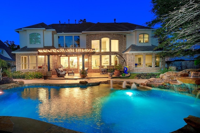 back of house at twilight featuring a patio area, brick siding, an outdoor pool, and stucco siding