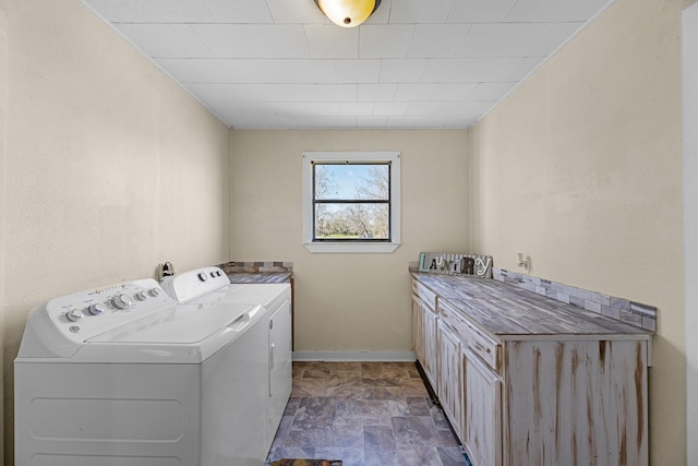 laundry area featuring baseboards, cabinet space, independent washer and dryer, and stone finish floor