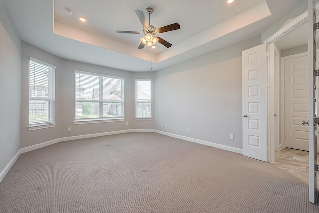 spare room featuring light carpet, a tray ceiling, a ceiling fan, and baseboards