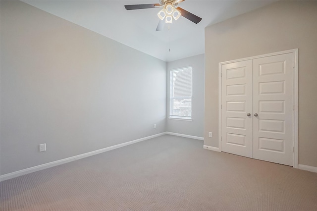 unfurnished bedroom featuring lofted ceiling, light colored carpet, a ceiling fan, baseboards, and a closet