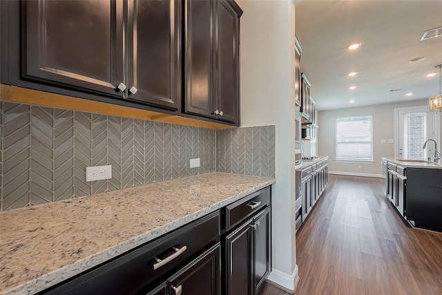 kitchen with dark wood-style flooring, a sink, backsplash, and light stone countertops