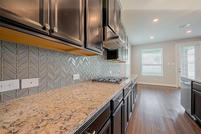 kitchen featuring light stone counters, under cabinet range hood, stainless steel appliances, visible vents, and decorative backsplash