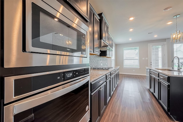 kitchen with stainless steel appliances, dark wood-style flooring, a sink, backsplash, and light stone countertops