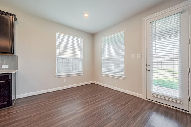 unfurnished living room featuring plenty of natural light, baseboards, and dark wood finished floors