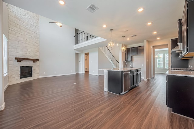 kitchen featuring a stone fireplace, dark wood-style flooring, visible vents, open floor plan, and an island with sink