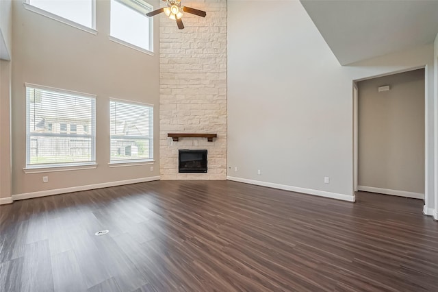 unfurnished living room featuring a stone fireplace, dark wood-style flooring, a towering ceiling, and a ceiling fan