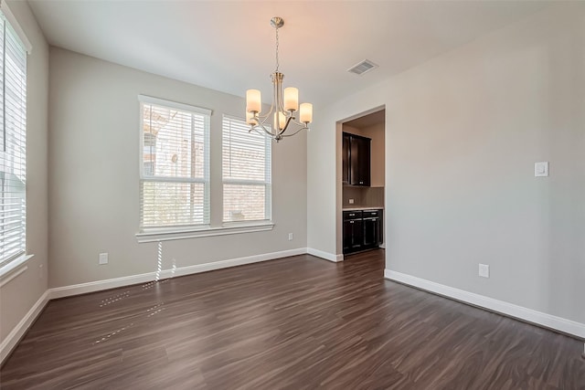 spare room featuring baseboards, dark wood-style flooring, visible vents, and an inviting chandelier