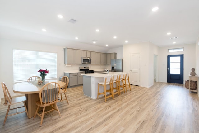 kitchen featuring an island with sink, gray cabinets, a kitchen breakfast bar, stainless steel appliances, and light wood-style floors