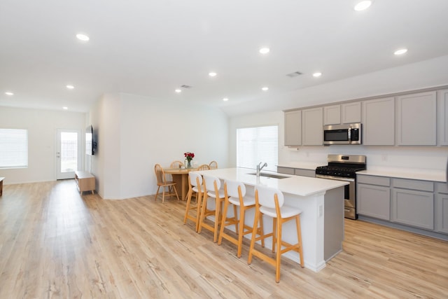 kitchen with gray cabinetry, an island with sink, light countertops, stainless steel appliances, and a sink