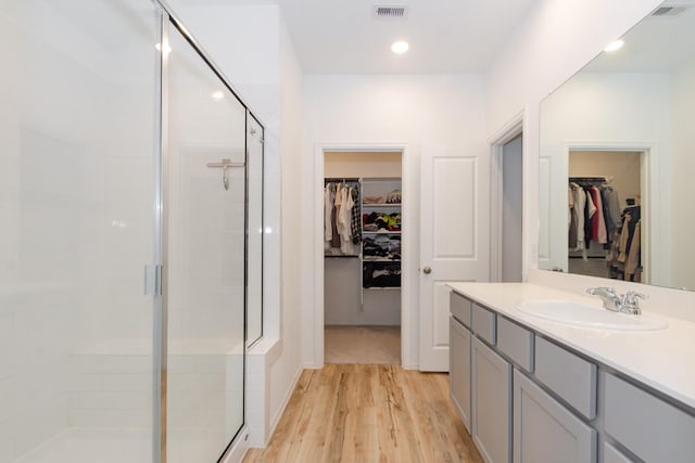 bathroom featuring visible vents, a walk in closet, wood finished floors, a shower stall, and vanity