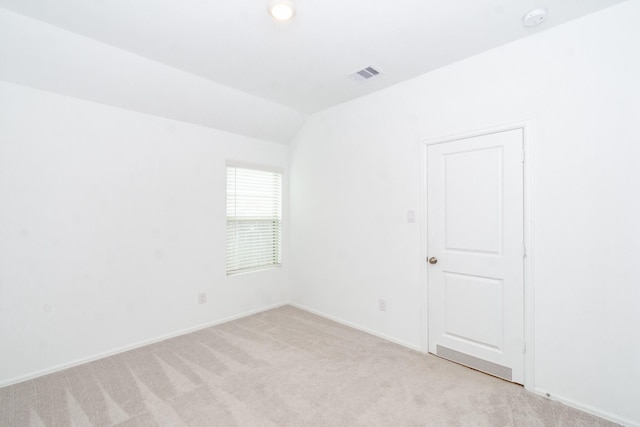 spare room with visible vents, light colored carpet, baseboards, and vaulted ceiling