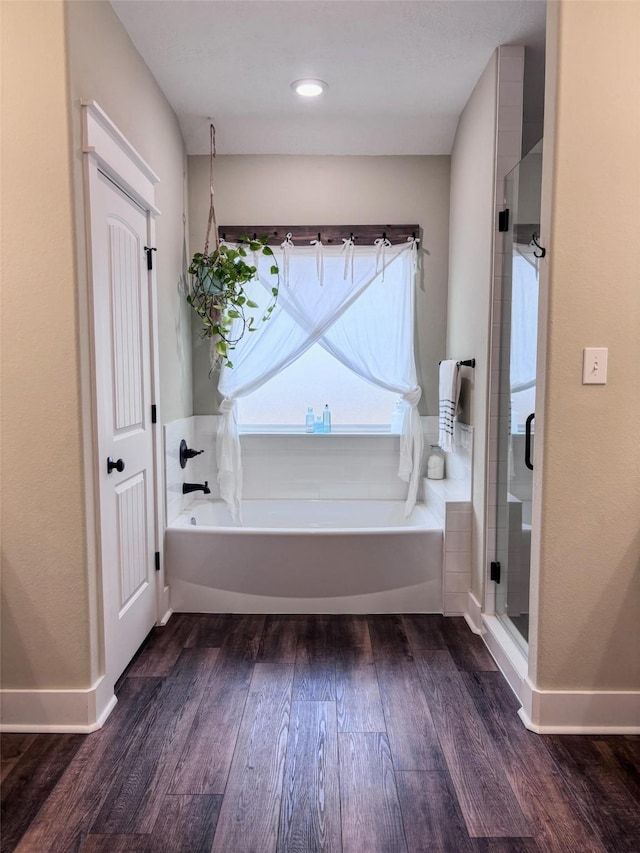 bathroom with a garden tub, a shower stall, baseboards, and wood finished floors